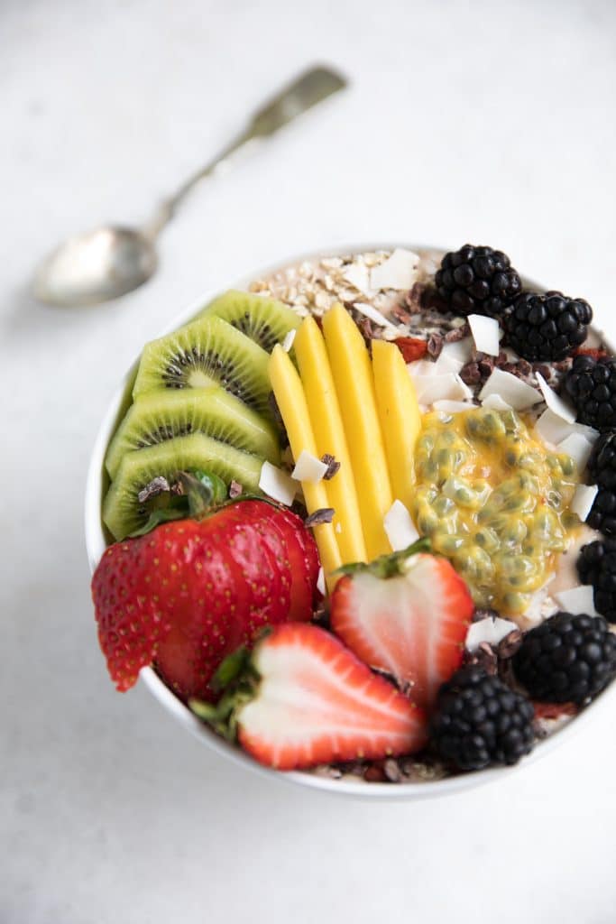 Thick strawberry yogurt smoothie in a white bowl topped with fresh fruit, coconut chips, and oats.