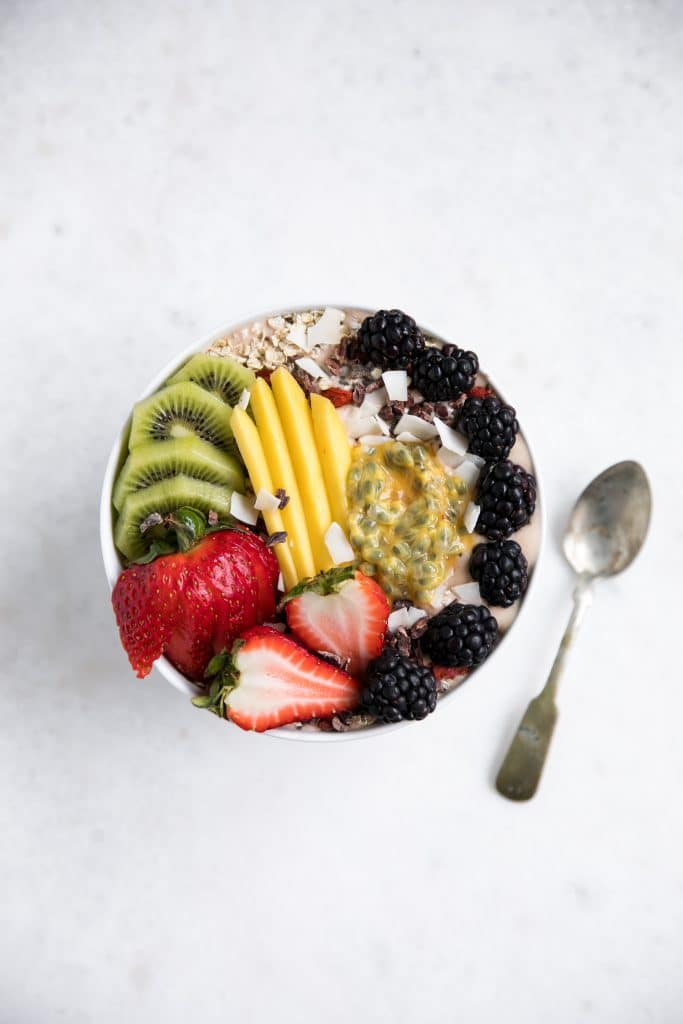 White bowl filled with strawberry and yogurt smoothie topped with fresh fruit.