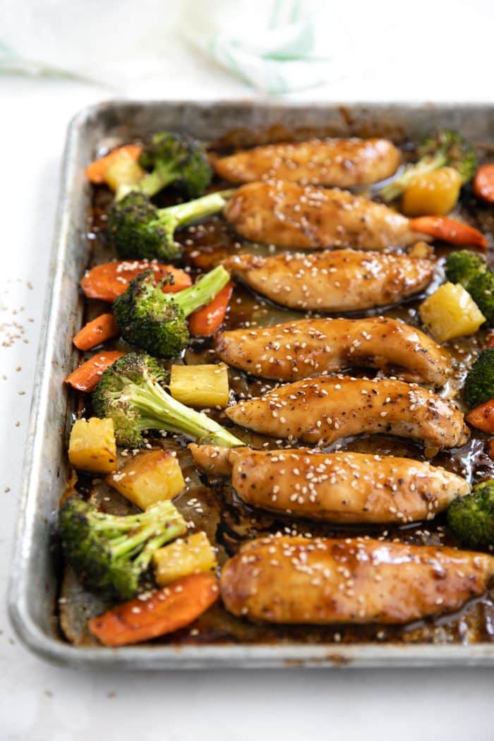 Roasted vegetables and chicken tenders on a baking sheet and covered in teriyaki sauce