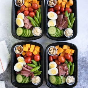 High protein snacks including cheese, egg, deli meat, hummus, and nuts in meal prep containers