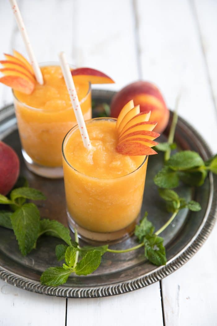 Wine slushies made with frozen peaches and white wine served in high ball glasses and garnished with fresh peach slices.