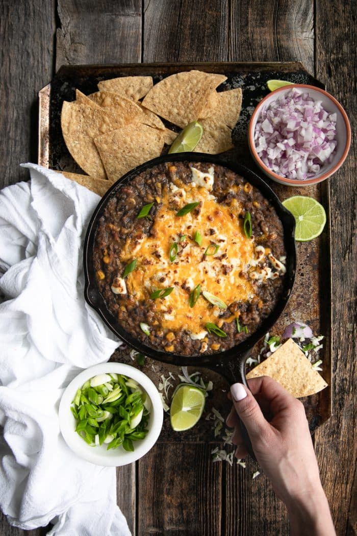 Overhead of girl holding a skillet filled with black bean dip surrounded by tortilla chips