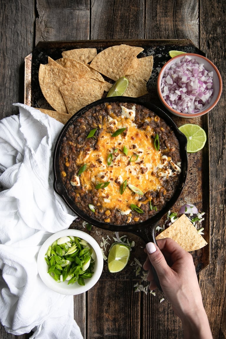 Overhead of girl holding a skillet filled with black bean dip surrounded by tortilla chips 