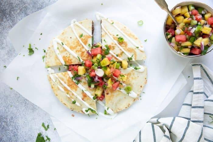 Overhead view of a cooked steak quesadilla next to a bowl of pineapple salsa