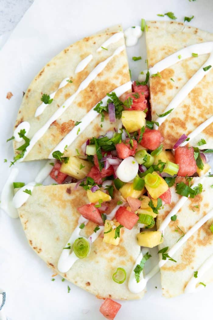 Overhead image of a perfectly golden steak quesadilla drizzled with sour cream, topped with fresh salsa, and sliced into four equal-sized quarters.