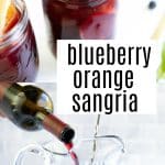 Mason jars filled with blueberry orange sangria, garnished with fresh mint and blueberries, surrounded by orange slices. A pitcher of sangria being poured from a bottle of red wine, with citrus fruits and blueberries nearby.