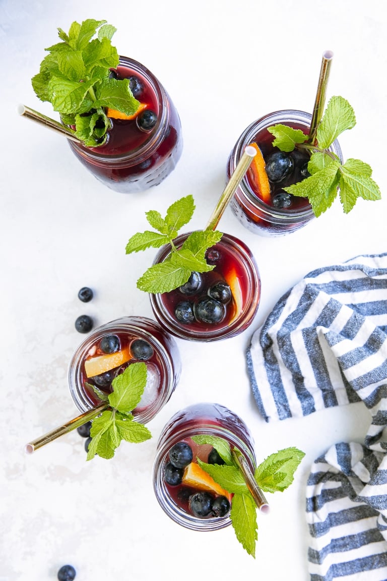 Flat-lay image of five glasses filled with Blueberry Sangria and garnished with mint
