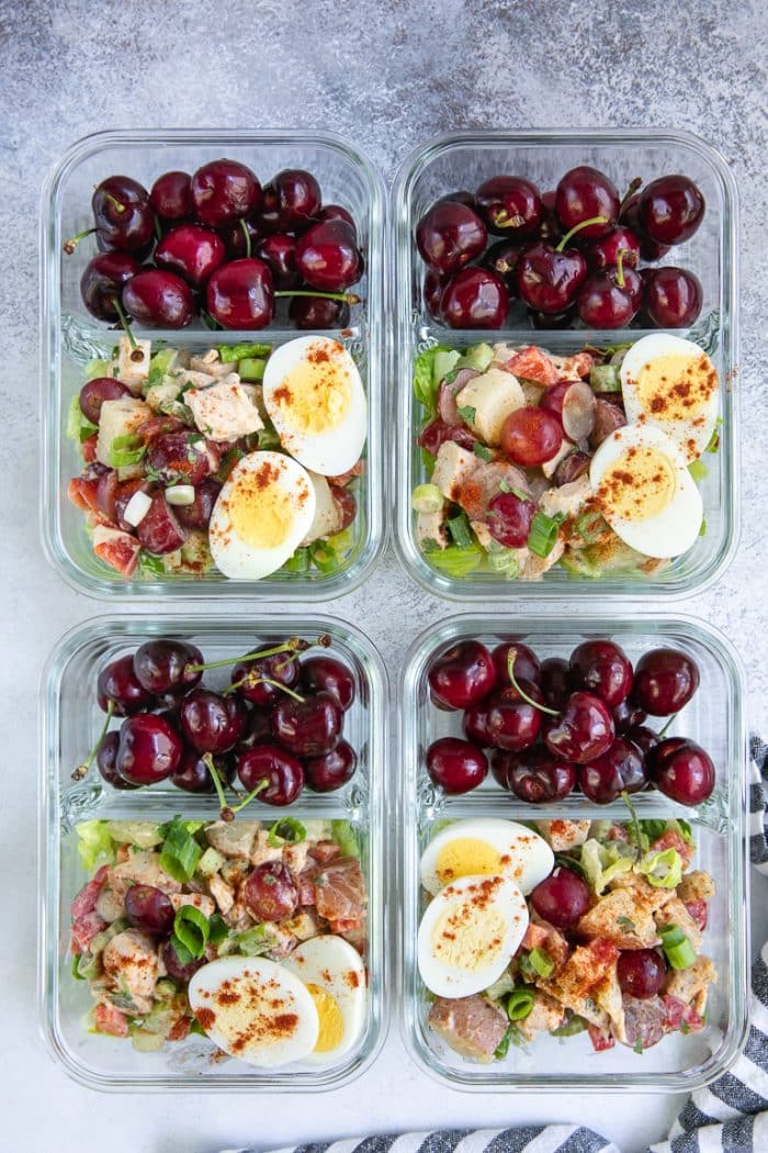 Four trays filled with chicken potato salad meal prep and topped with hard boiled egg.
