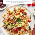 Pinterest pin image for Mediterranean Chickpea Salad with a white text box overlay reading โMediterranean Chickpea Saladโ and TheForkedSpoon.com over a plated chickpea salad with cucumber, tomatoes, red onion, Kalamata olives, feta cheese, parsley, lemon, dressing, and a rust-colored napkin.