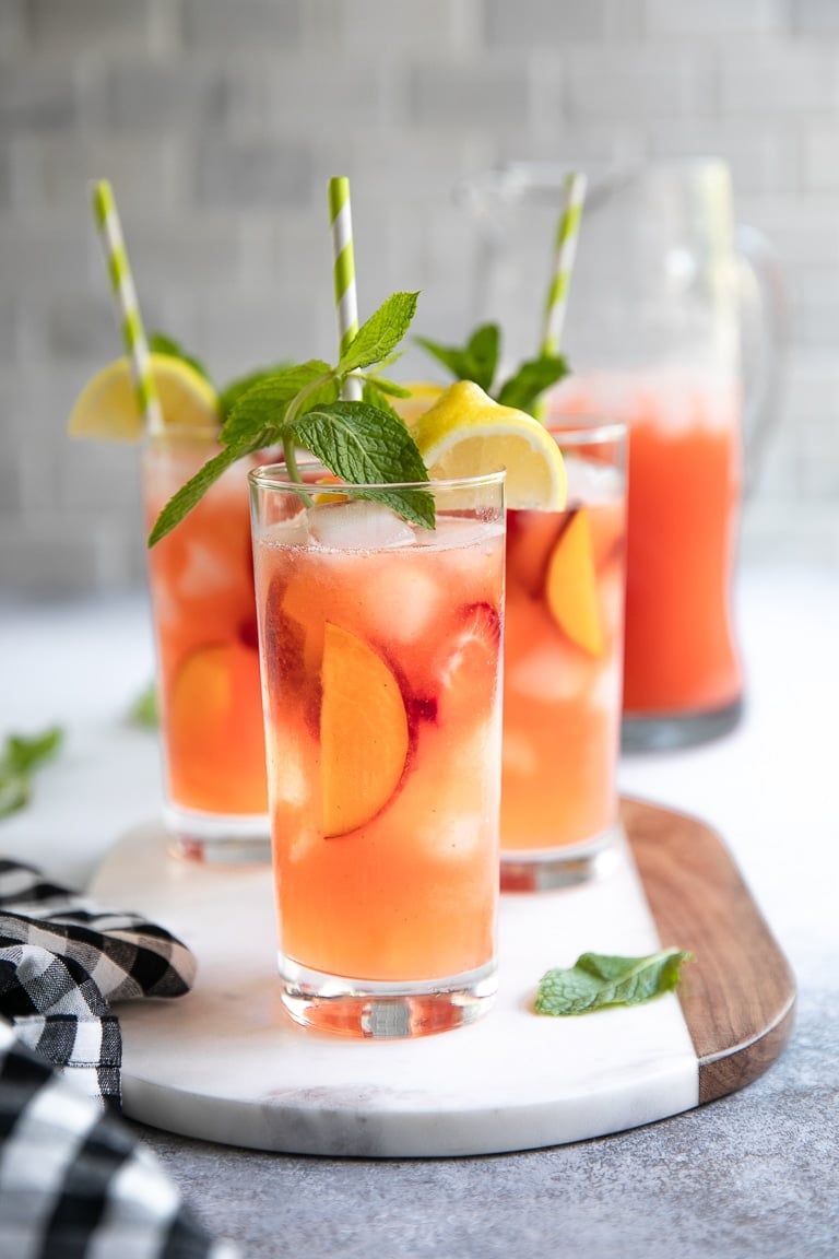 Tall glasses filled with peach and strawberry lemonade garnished with fresh mint.