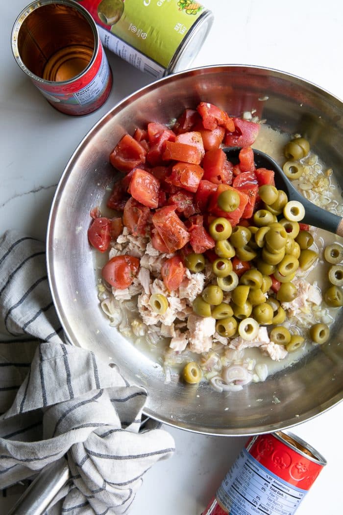 Skillet filled with simmering chunks of chicken, tomatoes, and green olives