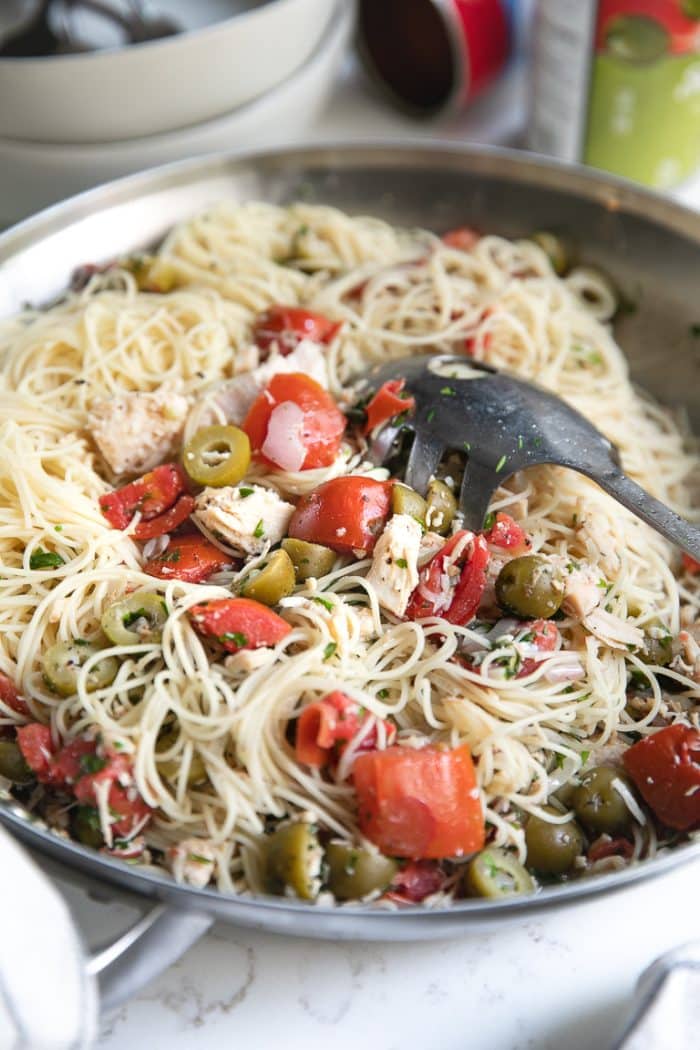 Side shot of Angel Hair Pasta with tomatoes, green olives, and chicken mixed together in a large skillet