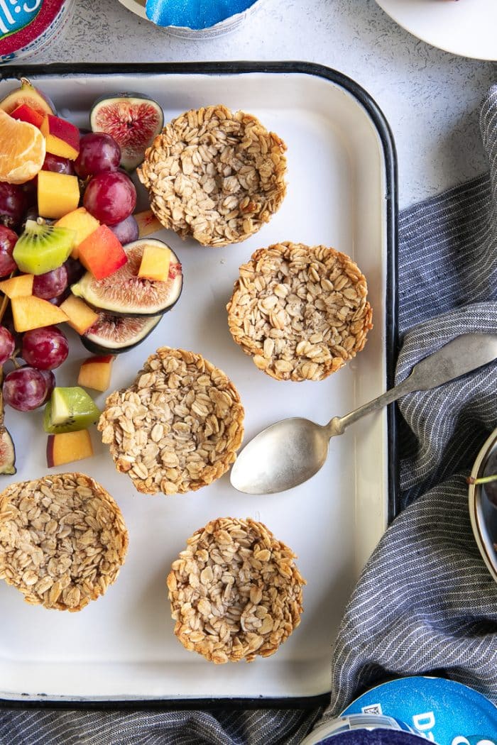 Overhead image of a white tray topped with golden baked oatmeal cups and a side of fresh chopped fruit.
