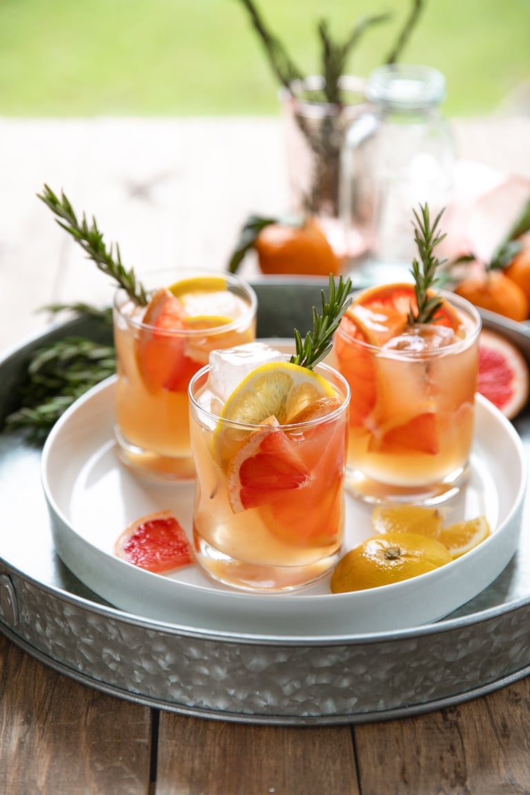 Tray with three glasses filled with Bourbon and grapefruit cocktail with rosemary