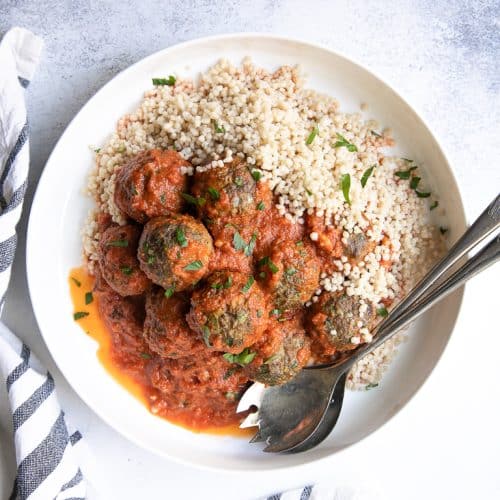 Large round serving dish filled with Middle Eastern Lamb Meatballs in a Saffron tomato sauce on a bed of cooked couscous.