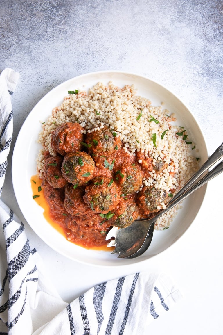 Large round serving dish with curried lamb meatballs covered in a saffron tomato sauce and served on top of couscous.