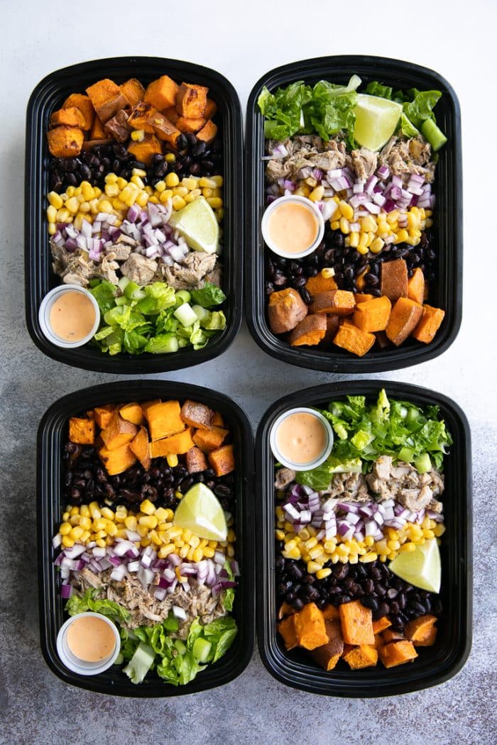 Four Meal Prep Bowls filled with roasted sweet potatoes, pork green chili, corn, beans, lettuce, and onion.