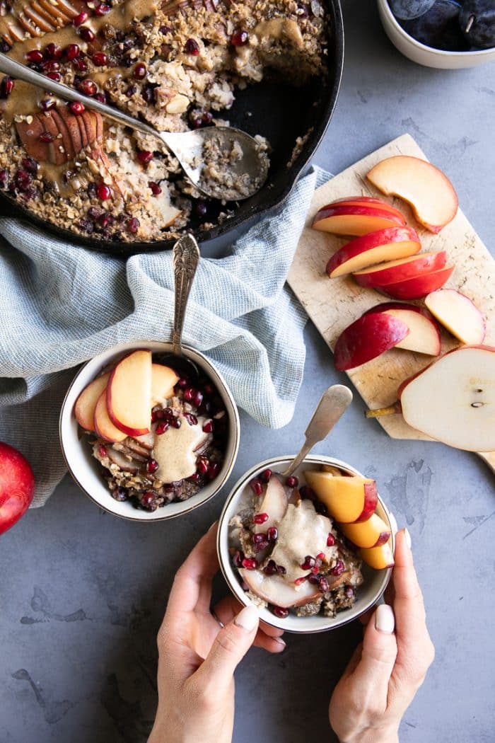 Two small bowls filled with baked oatmeal, fresh sliced fruit, and nut butter.