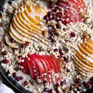 Cast iron skillet filled with rolled oats mixed with milk, pears, fruit, seeds, and nuts.