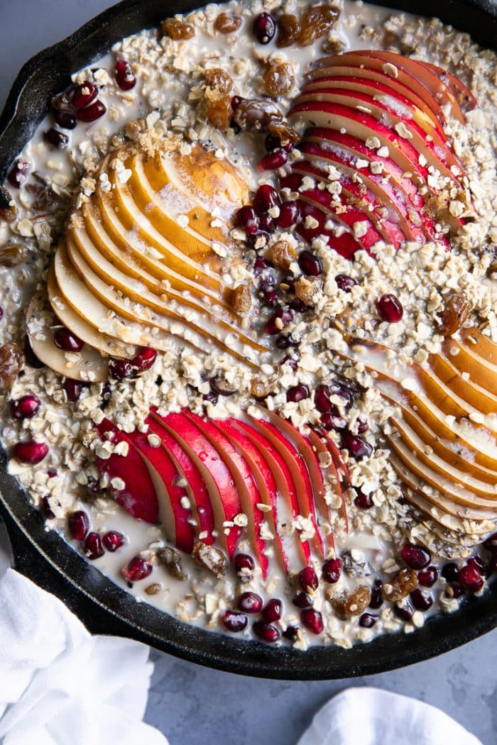 Cast iron skillet filled with rolled oats mixed with milk, pears, fruit, seeds, and nuts.
