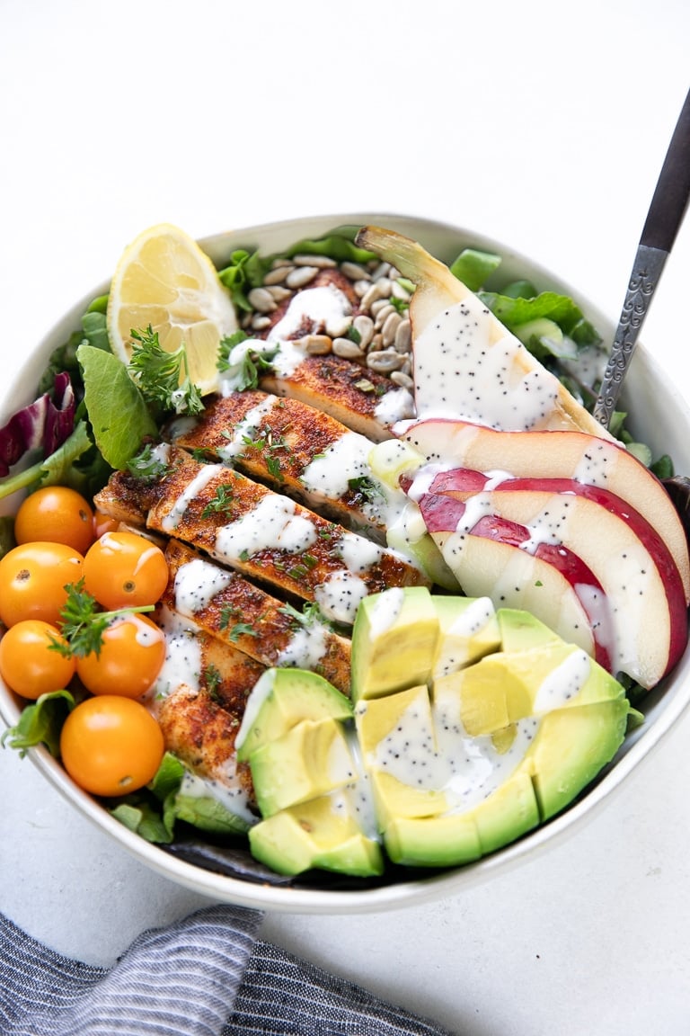Back-lit image of autumn chicken salad filled with pears, avocado, sunflower seeds, tomatoes, and poppyseed dressing
