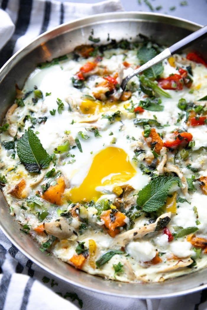 Egg frittata in a large skillet with butternut squash, bell peppers, and fresh herbs