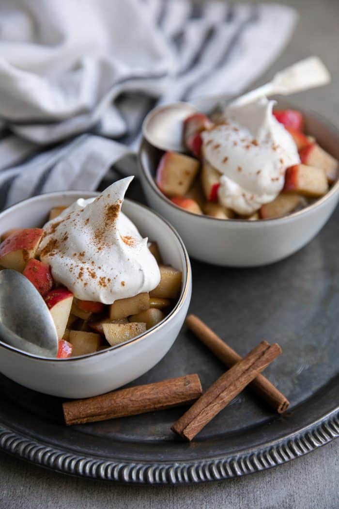 two bowls filled with fried apples and and topped with whipped cream and sprinkled with cinnamon