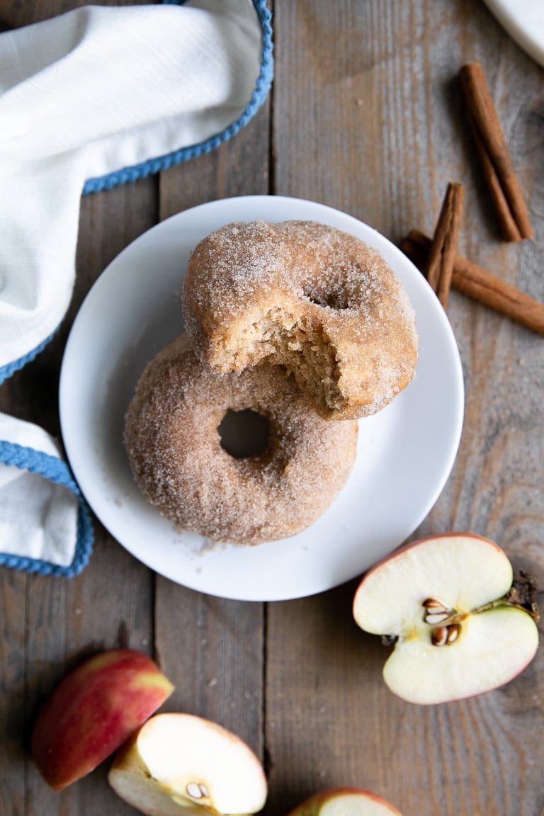 Two apple doughnuts on a white plate, one with a bite taken out of it.