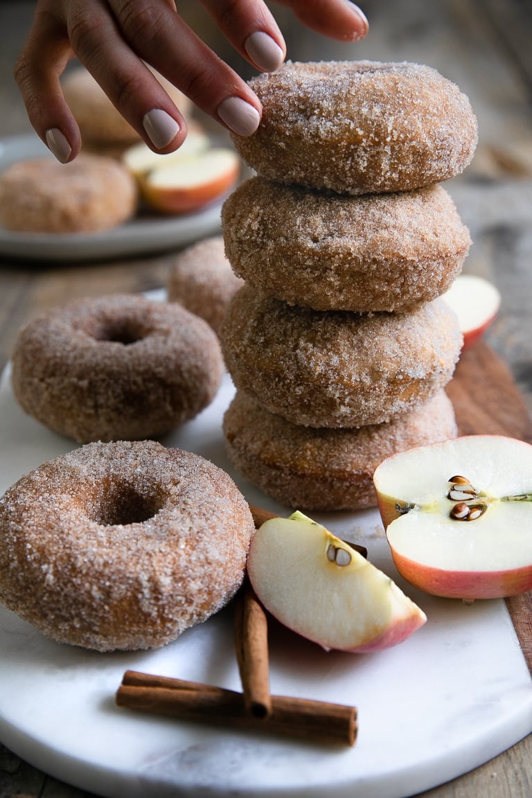 Stack of four Cinnamon Sugar Baked Apple Donuts on a small cutting board.