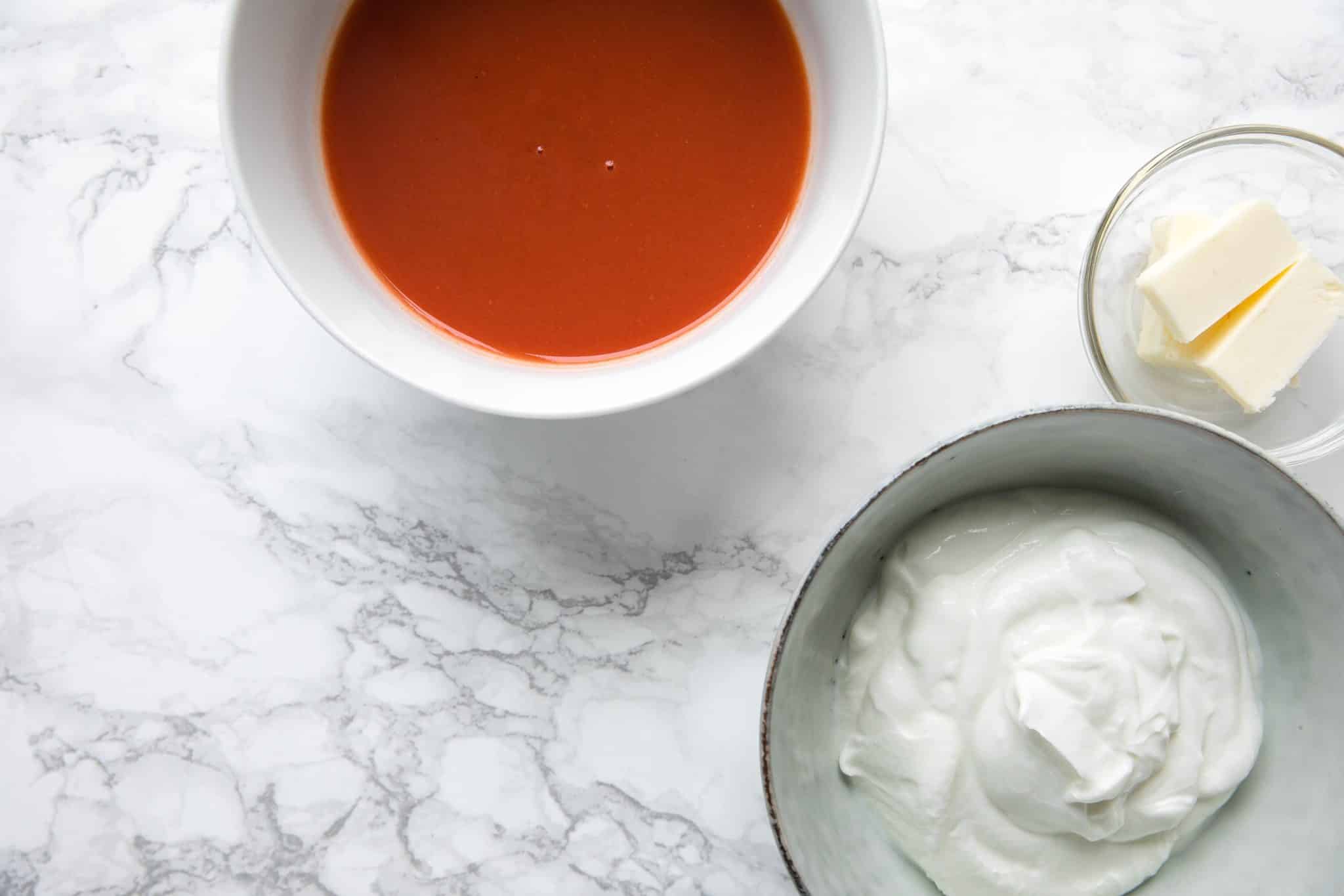 Three separate bowls. One containing hot sauce, one containing Greek yogurt, and one containing butter.