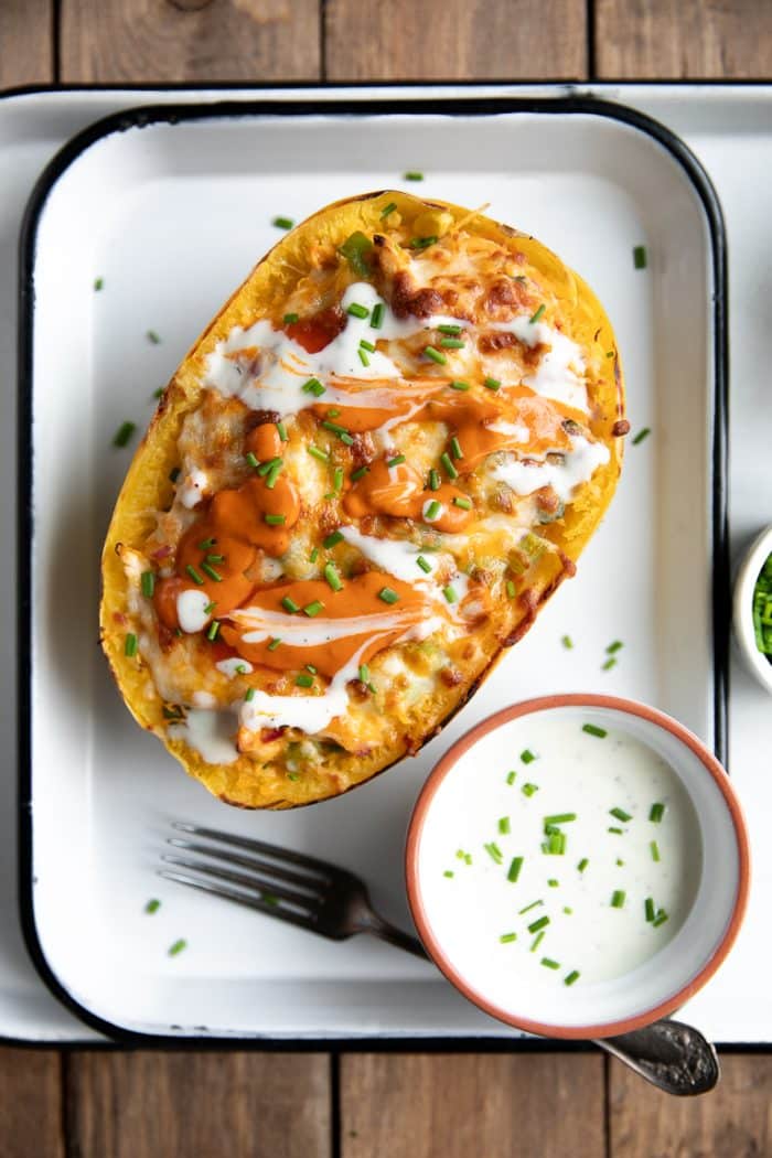 Cheesy bake buffalo chicken spaghetti squash topped with fresh chives and served on a white tray with a side of Ranch dressing.