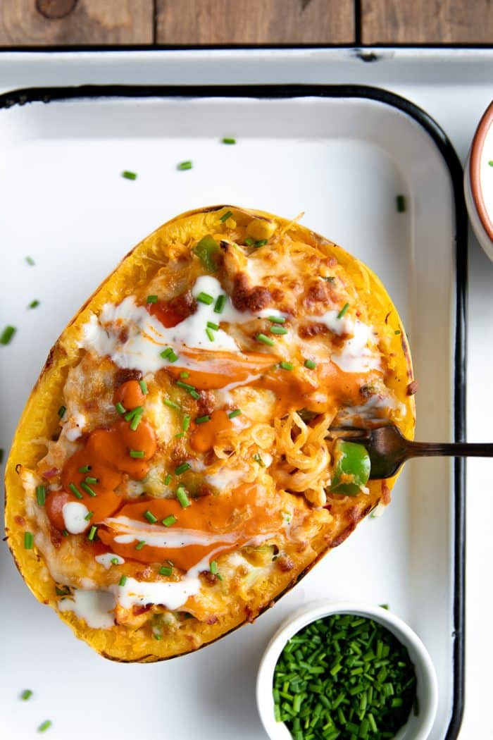 Fork digging into a Buffalo chicken spaghetti squash boat drizzled with ranch and chives
