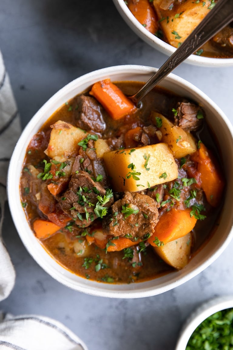White bowl filled with beef stew made of carrots, beef, potatoes