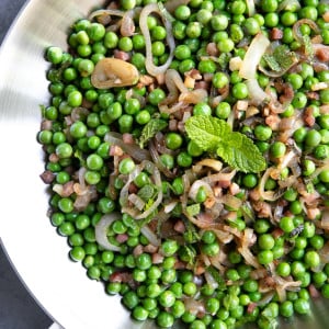 Large skillet filled with sauteed pancetta and shallots with cooked sweet peas and garnished with mint.