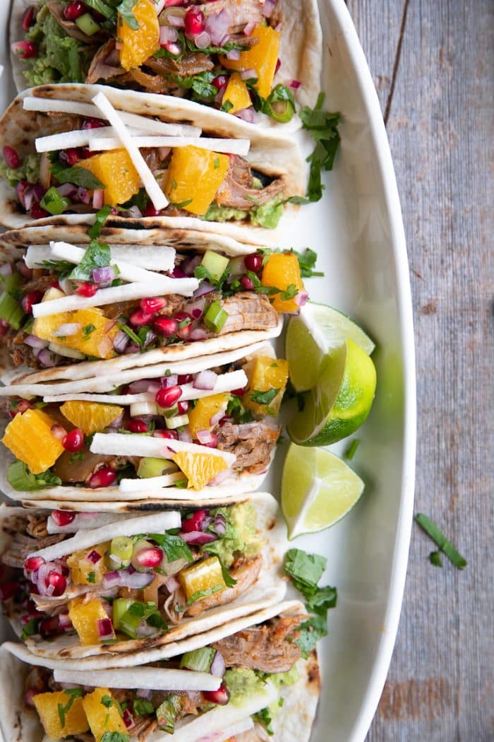 Six prepared harissa lamb tacos with pomegranate salsa all stacked in a row.