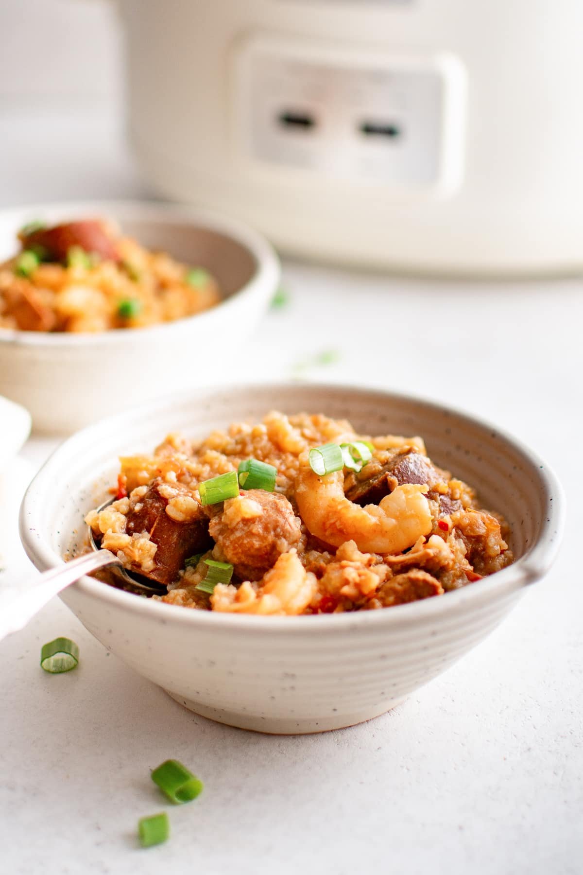 Slow cooker jambalaya served in ceramic bowls, topped with green onions with the white slow cooker in the background.