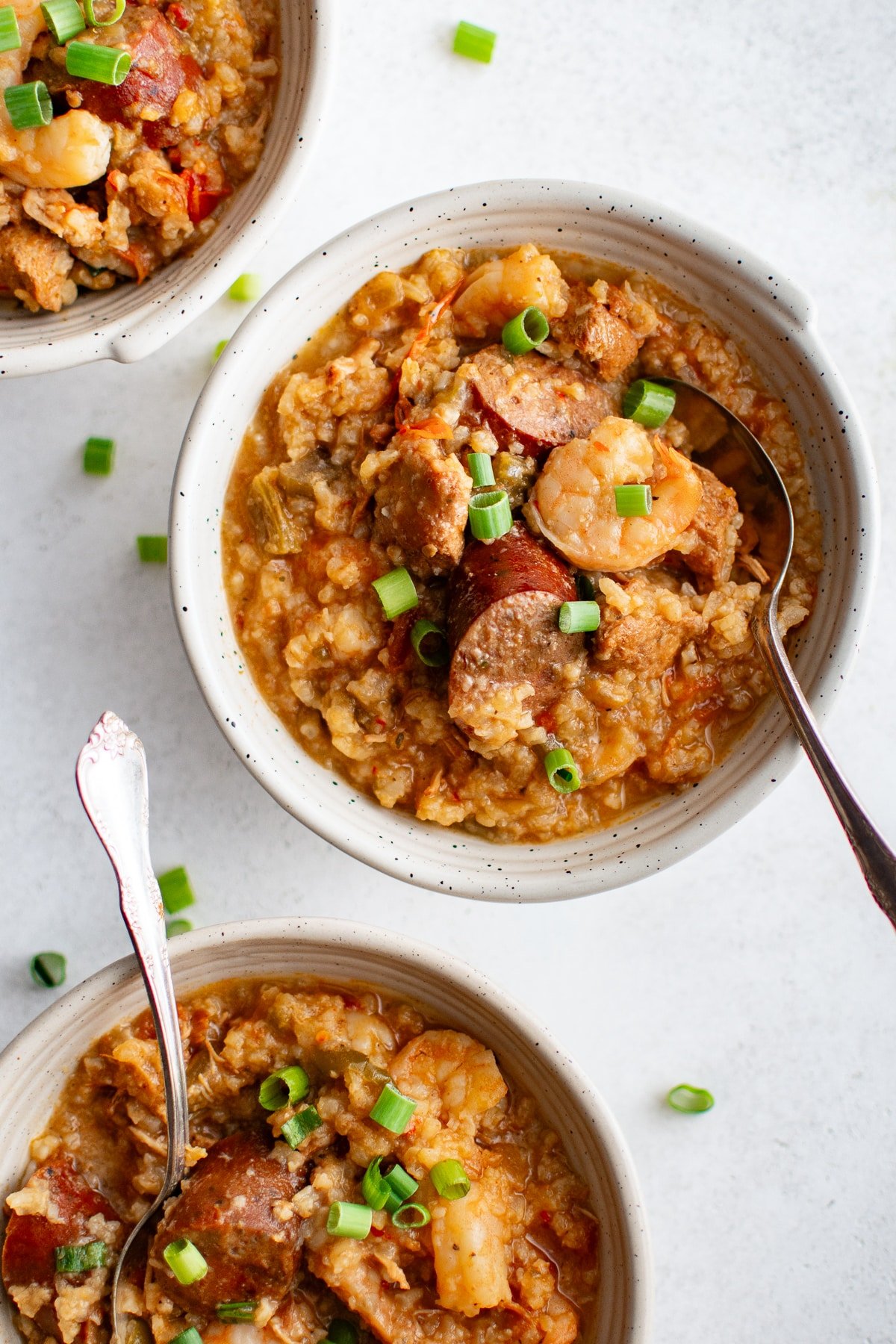 Three bowls of slow cooker jambalaya topped with green onions and filled with shrimp, sausage, and rice.