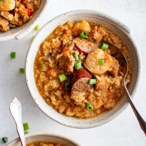 Three bowls of slow cooker jambalaya topped with green onions and filled with shrimp, sausage, and rice.