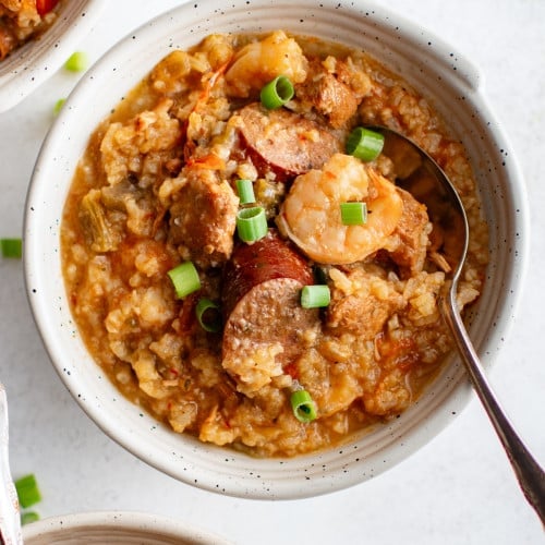 Three bowls of slow cooker jambalaya topped with green onions and filled with shrimp, sausage, and rice.