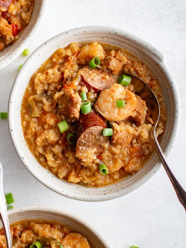 Three bowls of slow cooker jambalaya topped with green onions and filled with shrimp, sausage, and rice.