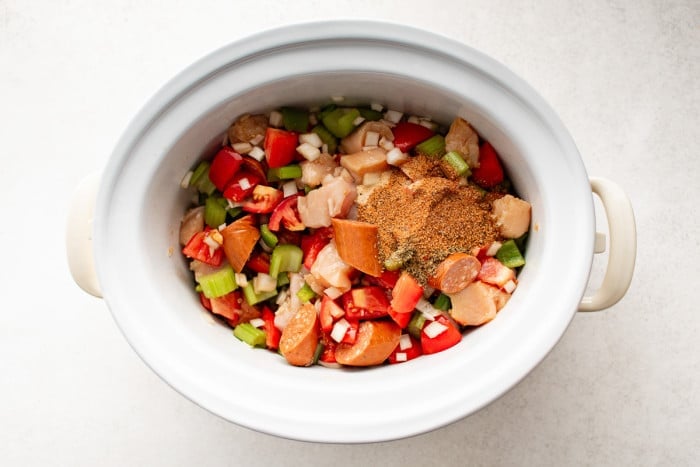 Seasonings added to jambalaya ingredients in a slow cooker before stirring.