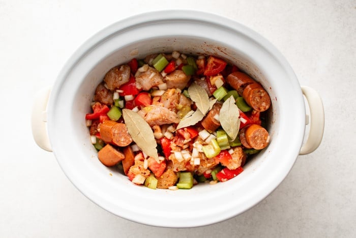 All ingredients stirred together in the slow cooker for jambalaya and topped with bay leaves.