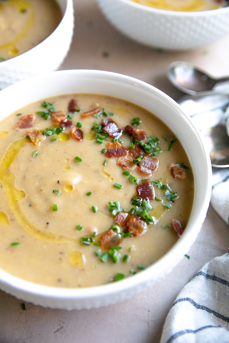 White bowls filled with dairy-free leek and potato soup topped with bacon bits and chives