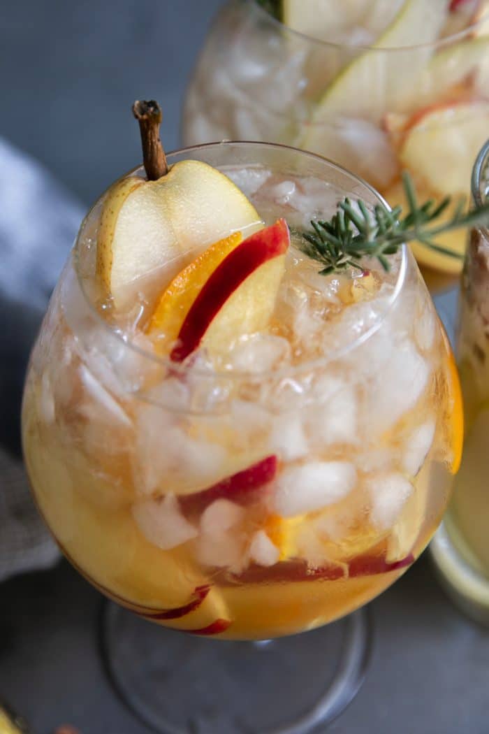 Large glass goblet filled with fall sangria made with white wine, pear liqueur, apples, pears, and oranges.