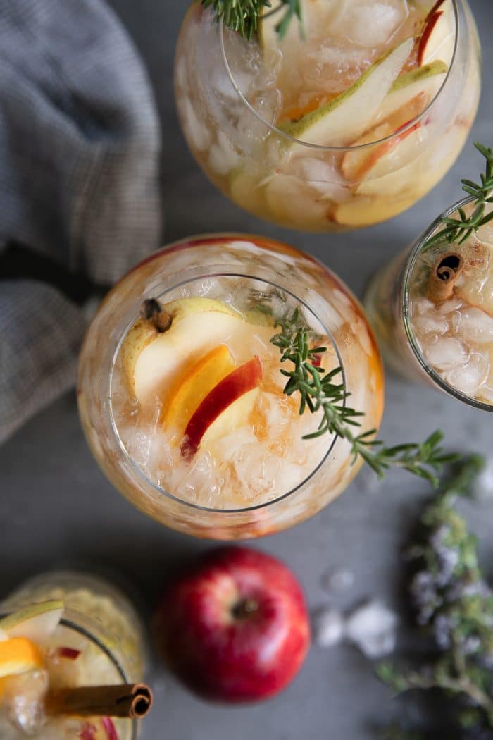 Overhead image of four glasses filled with iced pear and apple autumn sangria garnished with rosemary and pear