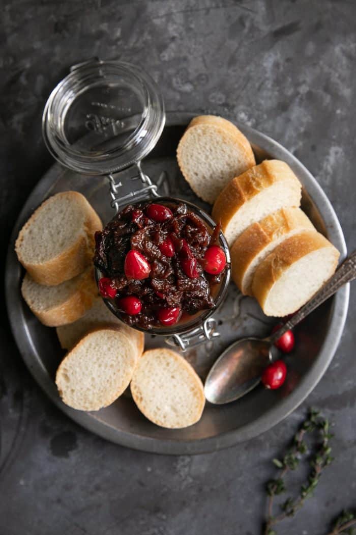 Overhead image of a tin pie dish holding a jar filled with cranberry bacon jam and sliced baguette