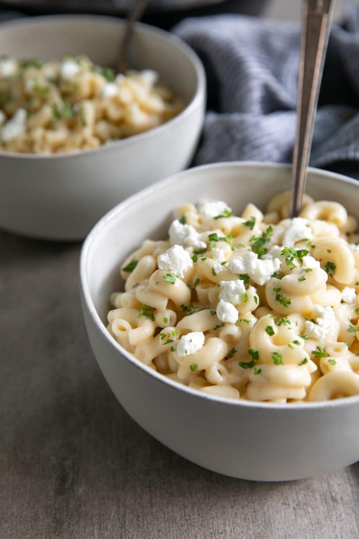 Two bowls filled with creamy mac and cheese and topped with goat cheese and parsley.