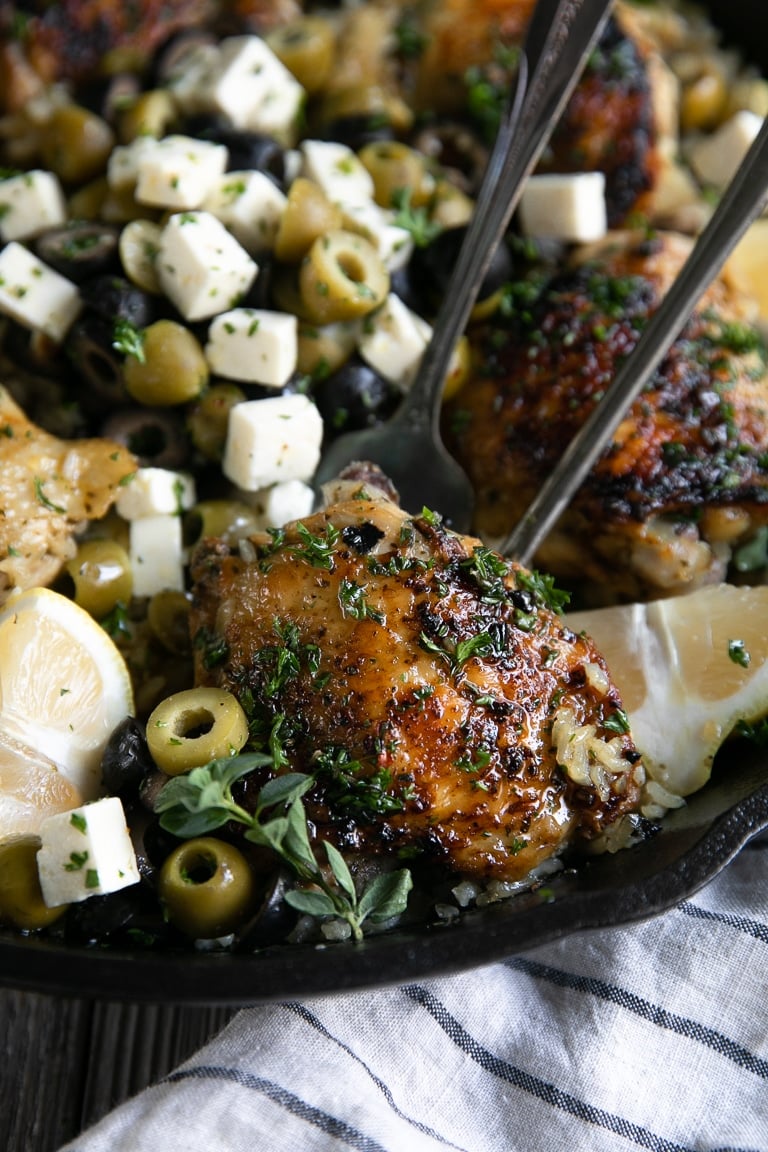 Bone-in skin-on chicken thigh cooked with rice and olives in a large cast iron pan in the oven.