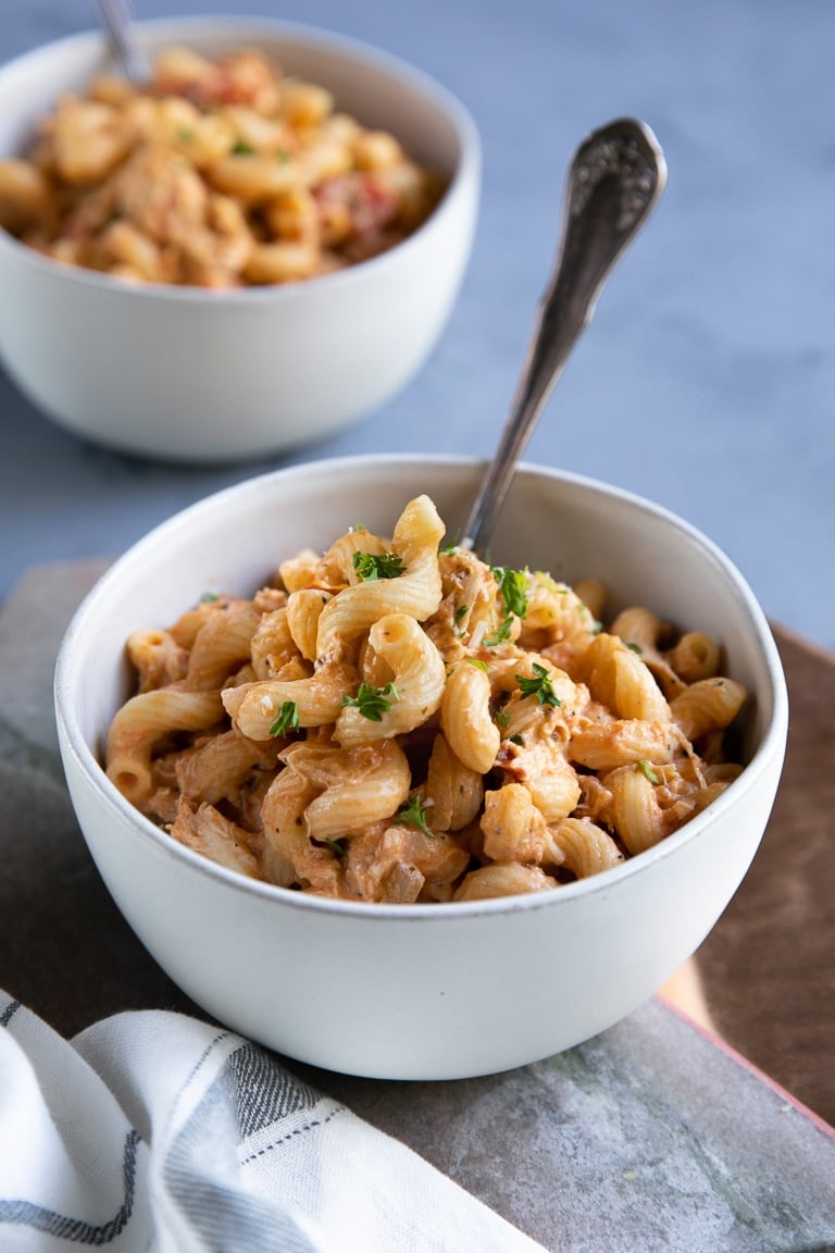 close-up image of creamy chicken pasta in a white bowl plus bowl of pasta in the background.