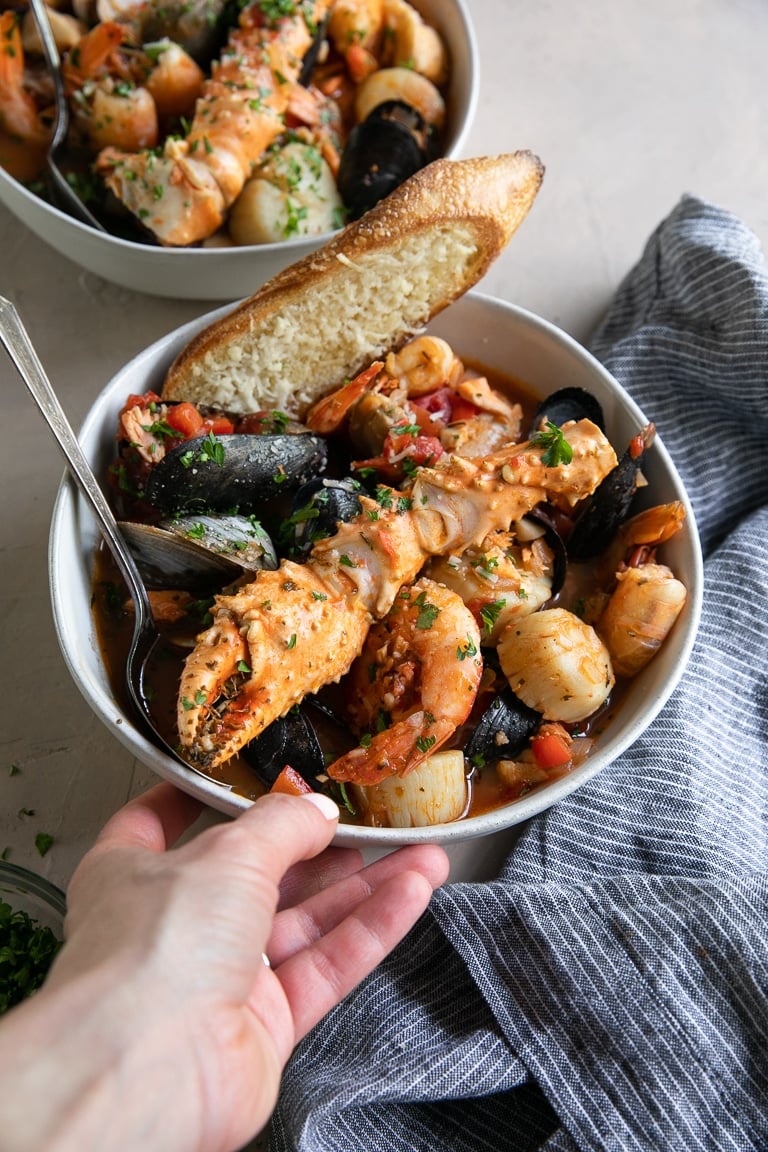 A bowl Cioppino seafood stew filled with shrimp, scallops, crab legs, fish, clams, and mussels and served with slices of bread.